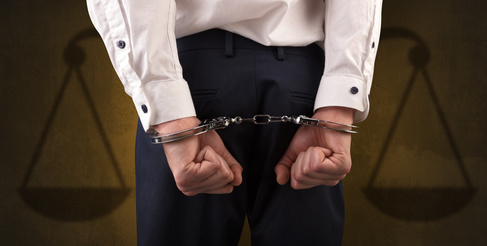 Arrested businessman in handcuffs with hands behind back and justice symbol wallpaper