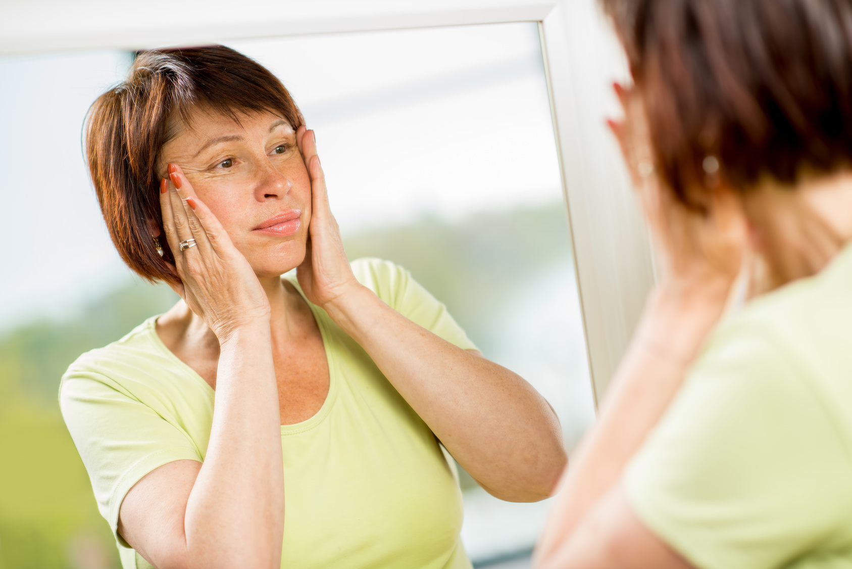 Sad older woman looking at her face into the mirror worried about the wrinkles