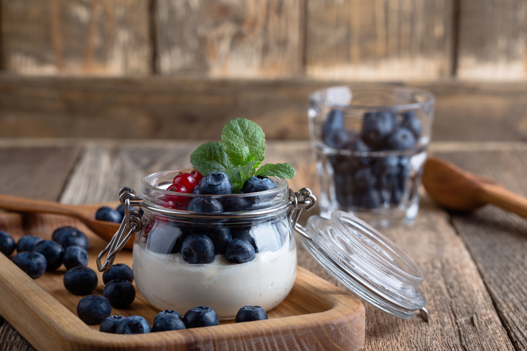 Cheesecake creme parfaits with blueberries and red currant berries served in jar, delicious summer no-bake dessert on rustic wooden table ready to eat